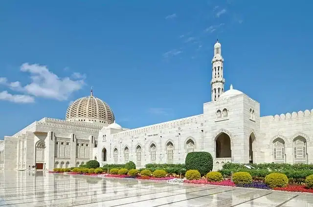 Vue sur la Grande Mosquée du Sultan Qaboos à Mascate, Oman, montrant le grand dôme doré et le minaret principal sous un ciel clair.