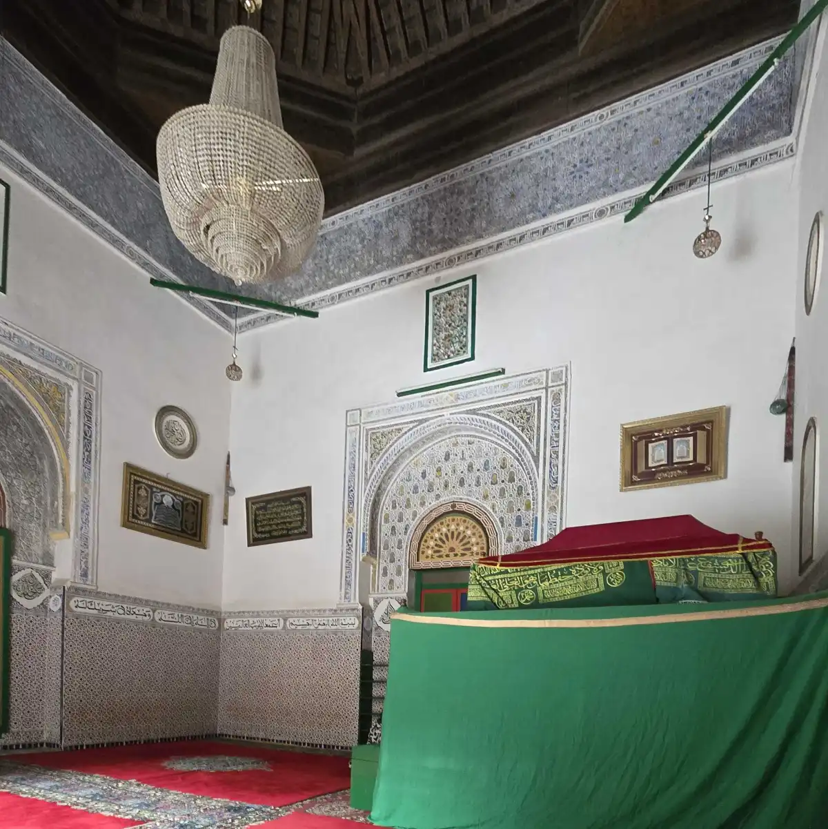 Interior wall decorated with intricate blue-and-white Islamic tile panels and framed artwork, plus a large woven chandelier hanging from the ceiling.