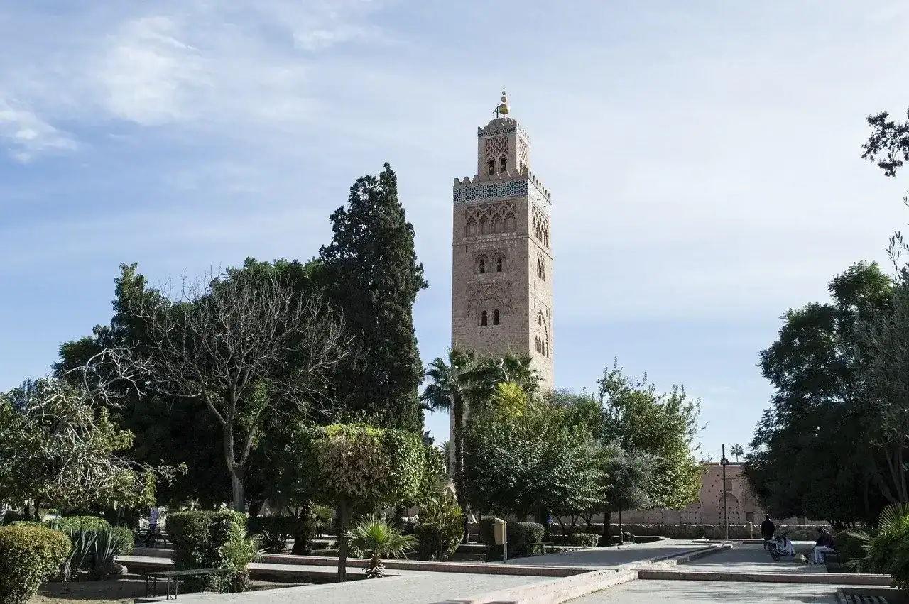 Minaret de la mosquée de la Koutoubia à Marrakech, entouré de jardins et de palmiers sous un ciel bleu.