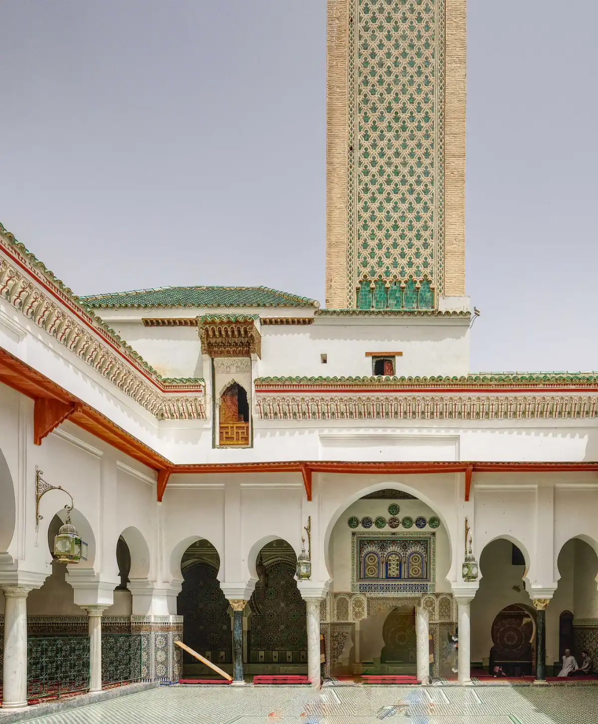 patio-interieur-minaret-mosquee-moulay-idriss-fes Vue panoramique du patio intérieur de la mosquée Moulay Idriss II à Fès, montrant le minaret orné, les arcades blanches et le sol en zelliges géométriques.