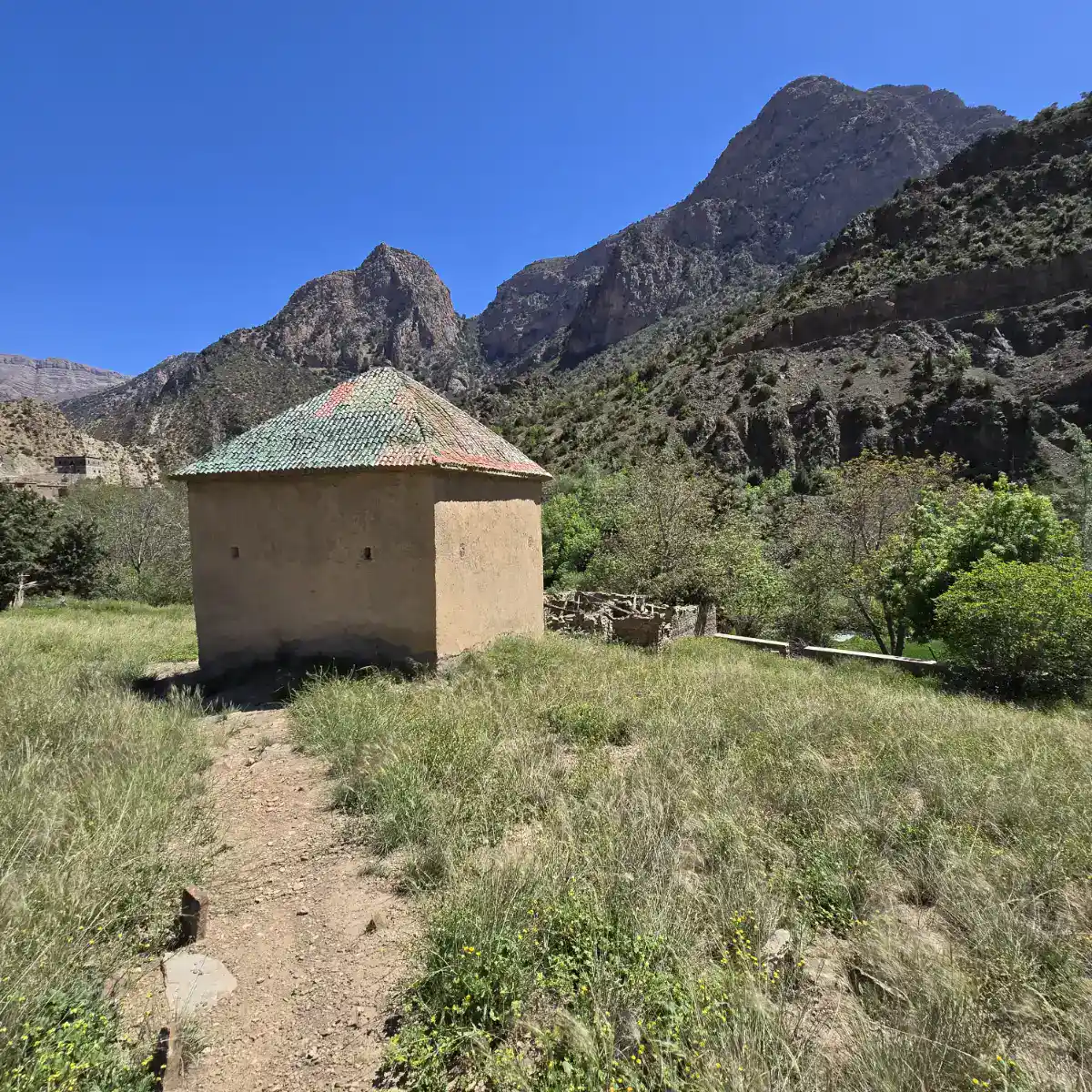 Vue panoramique du village de Zaouiat Ahansal dans le Haut Atlas, montrant l'architecture traditionnelle en pierre au pied des montagnes rocheuses.