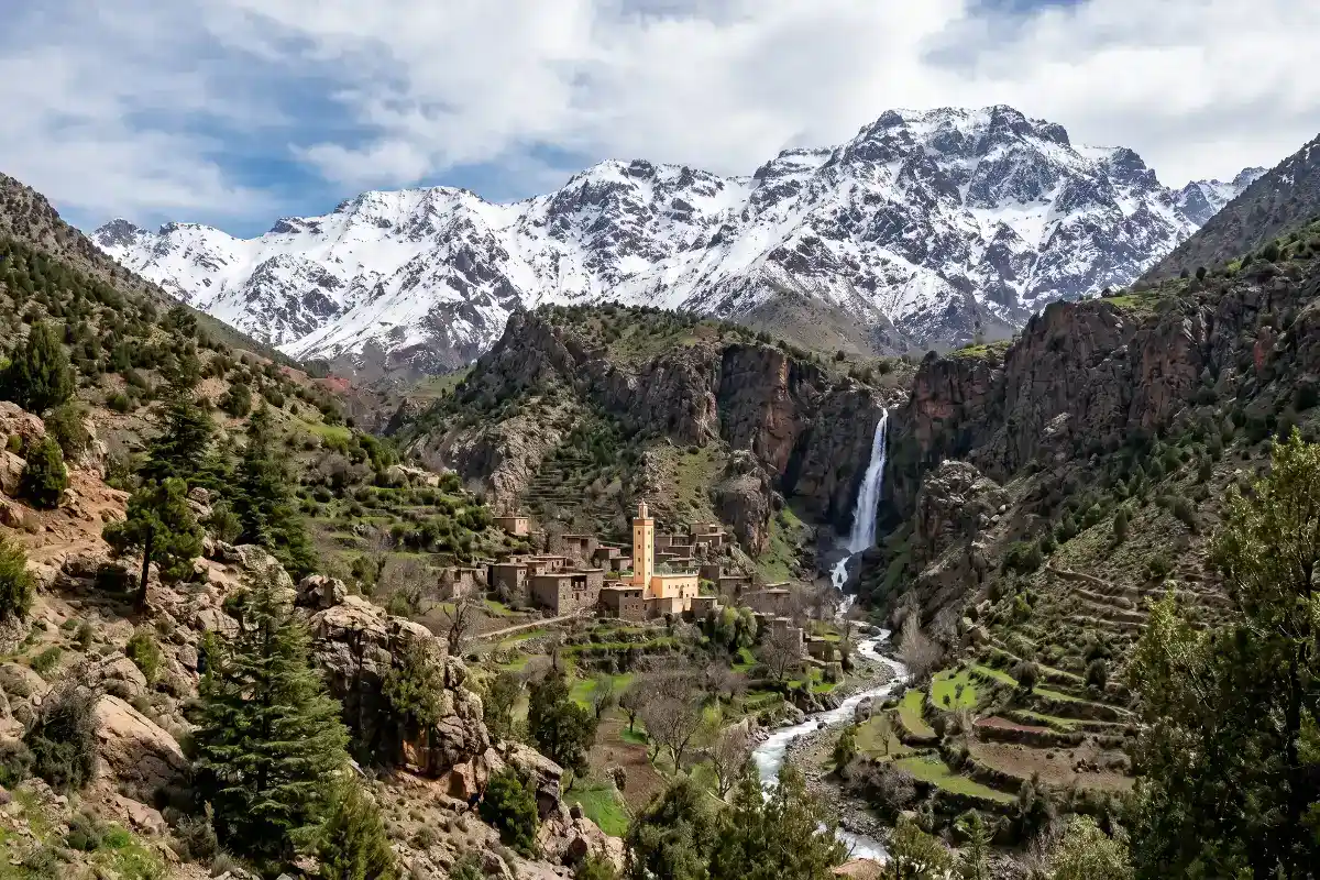 zaouiat-ahansal-spiritualite-haut-atlas-maroc Vue panoramique du village historique de Zaouiat Ahansal dans le Haut Atlas marocain, montrant l'architecture traditionnelle en pisé au pied d'une immense falaise rocheuse sous un ciel bleu.