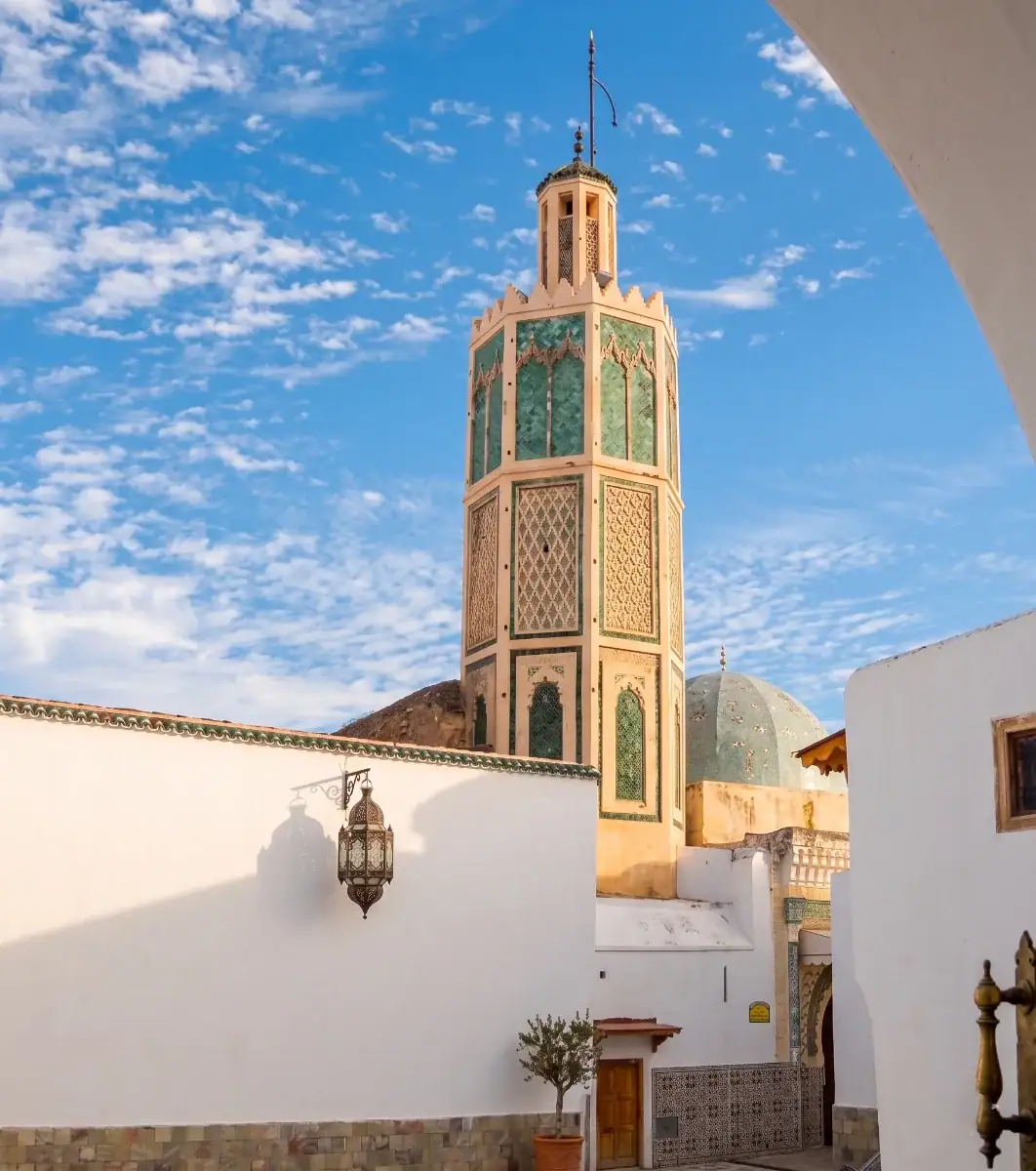 Minaret octogonal en zelliges verts et dôme de la mosquée de Dar Dmana dans une ruelle de la médina d'Ouezzane au Maroc sous un ciel bleu.