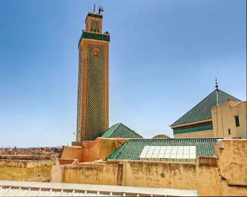Mausolée de Seïdina Ahmed Tijani - Fès Vue sur le minaret de la zaouïa de Seïdina Ahmed Tijani à Fès, orné de zelliges verts, s'élevant au-dessus des toits de la médina sous un ciel bleu.