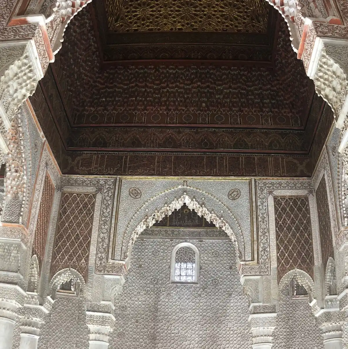 Architecture intérieure des Tombeaux Saadiens à Marrakech Vue intérieure détaillée des Tombeaux Saadiens à Marrakech, montrant la richesse de l'architecture avec ses murs en stuc finement sculpté, ses arcades décorées de calligraphies et son magnifique plafond en cèdre ouvragé.