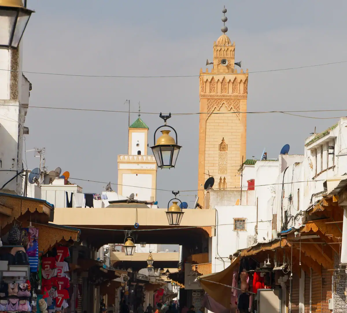 Ville de Rabat – Architecture et Héritage Almohade Rue animée de la médina de Rabat surmontée d'un minaret traditionnel en brique, symbole de l'architecture historique de l'Empire Almohade.