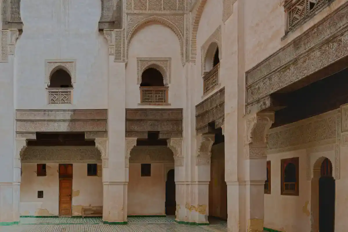 Médersa Bou Inania de Fès : Architecture et Cour Intérieure Vue détaillée de la cour intérieure de la Médersa Bou Inania à Fès, mettant en évidence les arcades sculptées en stuc, les fenêtres ornées de boiseries traditionnelles et le sol recouvert de zellige.
